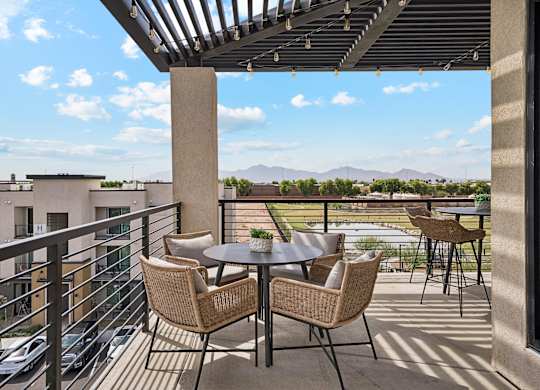A patio with a table and chairs overlooking a parking lot and buildings.
