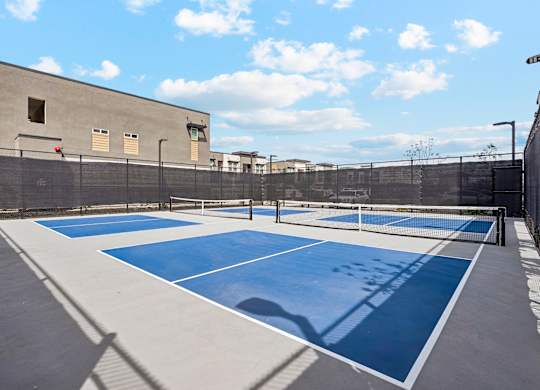 A tennis court with blue and white markings is surrounded by a fence and a building.