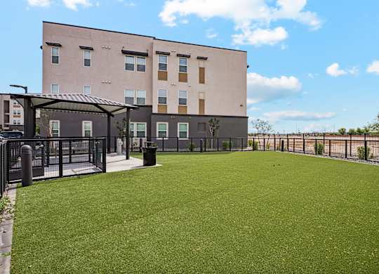 A large grassy area in front of a building with a fence and a small shelter.