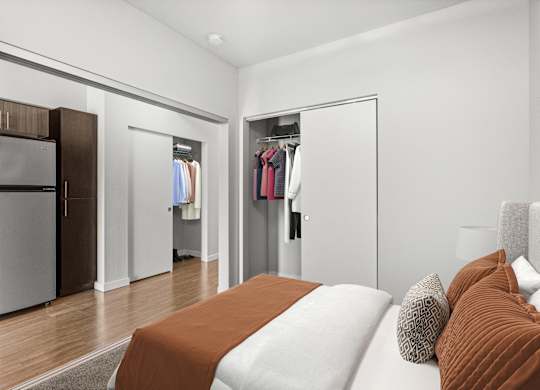 A bedroom with a bed, pillows, and a closet with clothes hanging.