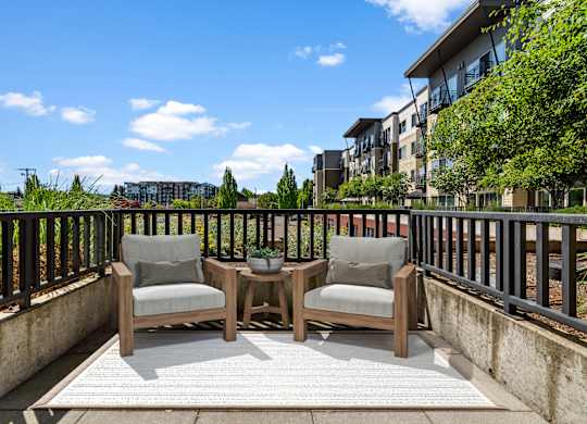 A balcony with two chairs and a table is set up on a sunny day.