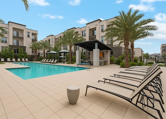 A pool area with sun loungers and a building in the background.