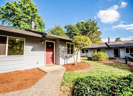 A house with a red door and a grey facade is surrounded by a green lawn and trees. at The Retreat, Sumner, 98390