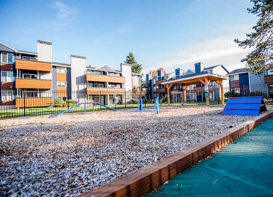 A playground with a blue slide and a pebble-covered area. at Northpoint Apartments, Washington, 98407