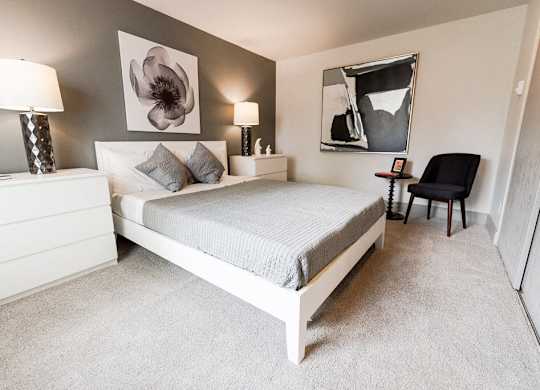 A bedroom with a bed, nightstand, lamp, and chair.