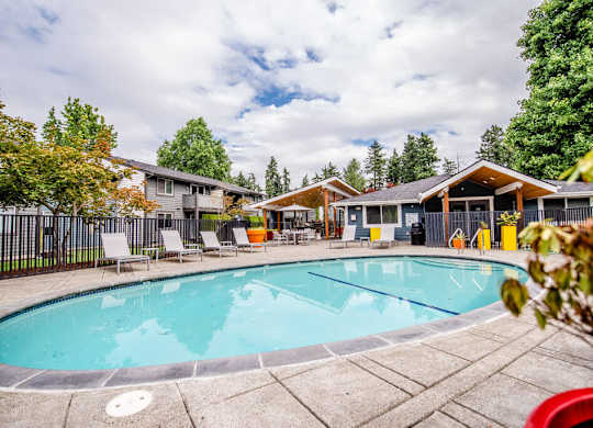 A swimming pool surrounded by trees and chairs.