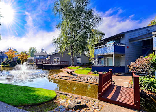 A sunny day at a park with a pond and a building in the background. at The Lakes at Fife, Fife, WA, 98424