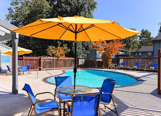 A yellow umbrella shades a table with blue chairs around a pool. at The Lakes at Fife, Fife, 98424