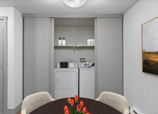 A kitchen with a dining table and chairs with a vase of red flowers on the table.