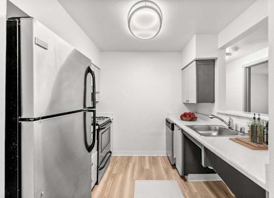 A modern kitchen with a refrigerator, sink, and wooden flooring.