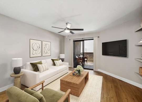 A living room with a white couch, a green chair, a wooden coffee table, and a flat screen TV mounted on the wall.