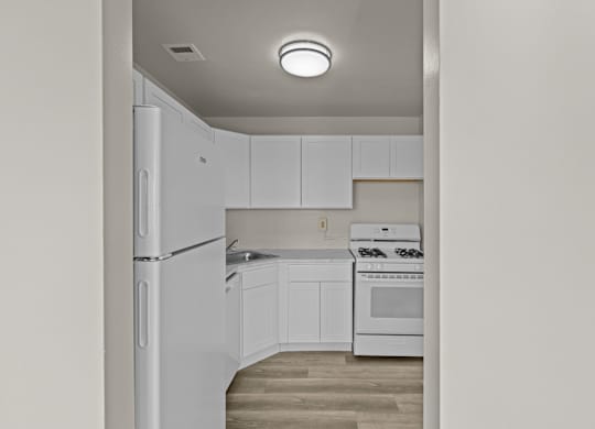 A white kitchen with a refrigerator, oven, and cabinets at Kensington House, Kensington, MD 20895
