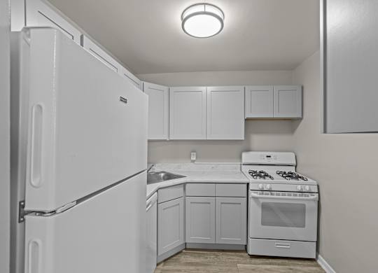 A white kitchen with a refrigerator, sink, stove, and cabinets at Kensington House, Maryland