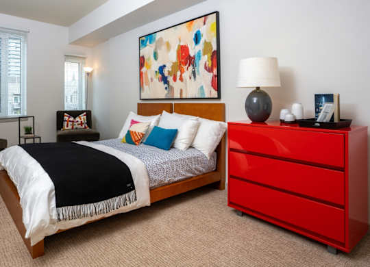 A bedroom with a large bed, a red dresser, and a painting on the wall.