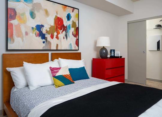 A bedroom with a large bed and a colorful painting above it.