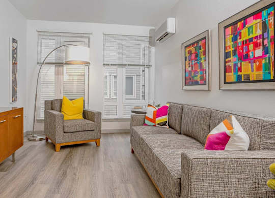 A living room with a grey couch, a yellow pillow on the chair and a painting on the wall.