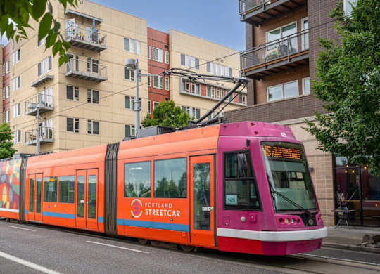 A streetcar with a pink and orange design is on a street.