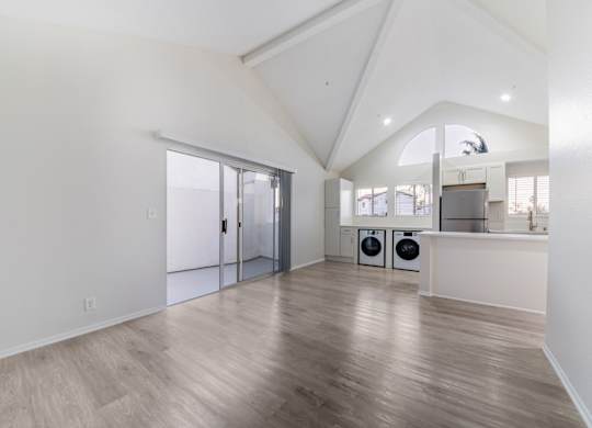 A spacious room with wooden flooring and a kitchen area in the background.