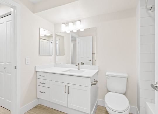 A white bathroom with a toilet, sink, and mirror.