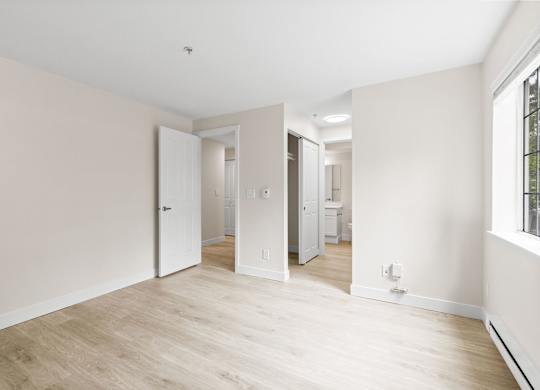 A room with white walls and wooden flooring with a doorway leading to another room.