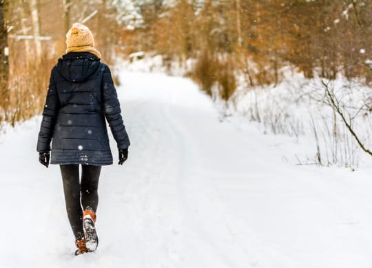 a woman walking in the snow in the woods