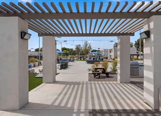 A white pergola with a striped floor and a picnic table underneath.