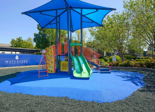 a playground with a blue umbrella and red and yellow slides