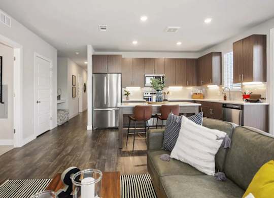 A modern kitchen and living room with a grey couch and wooden floors.