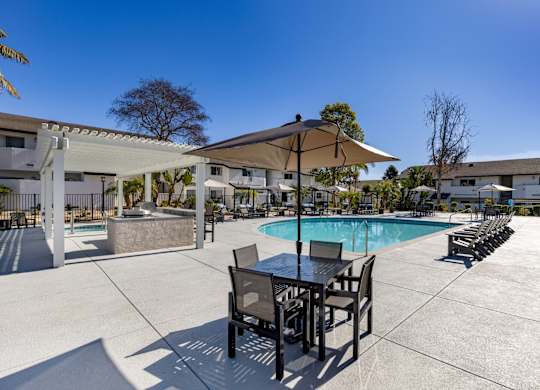A pool area with a table and chairs and a sun umbrella.