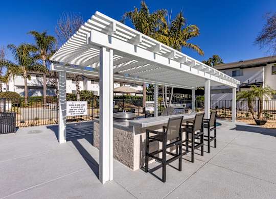 A white pergola with a table and chairs is set up in a sunny outdoor area.