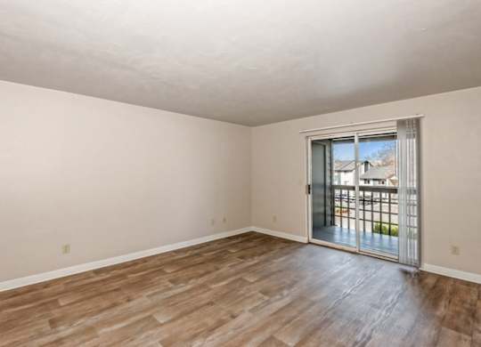 Empty room with wooden flooring and sliding glass door.