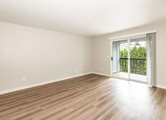 A room with wooden flooring and a sliding glass door leading to a balcony.