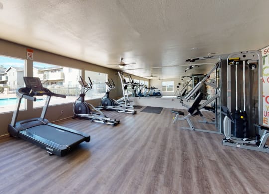 Fitness Center with Exercise Equipment and a Large Window Facing Toward the Pool at Aspire High Desert Apartments, Victorville