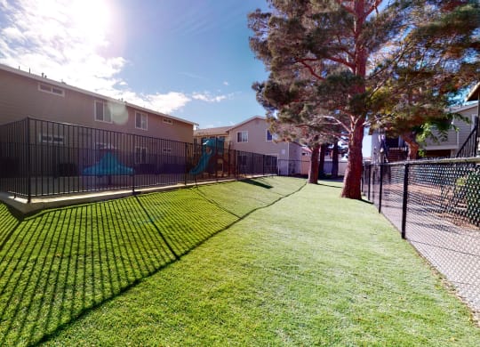 Fenced-In Playground Next to Apartment Building Surrounded by Lush Landscaping at Aspire High Desert Apartments, Victorville, California