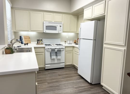 a kitchen with white cabinets and white appliances at Riverton of the High Desert Apartments,Victorville, CA