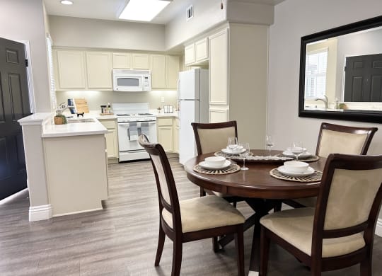 a dining area with a table and chairs and a kitchen in the background at Riverton of the High Desert Apartments, California, 92392
