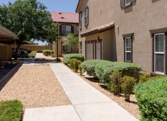 an exterior view of a building with a walkway and sidewalk at Riverton of the High Desert Apartments, Victorville, CA