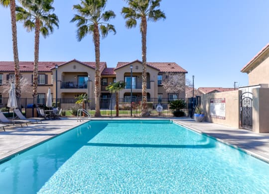 a swimming pool with palm trees and apartments in the background at Riverton of the High Desert Apartments, CA, 92392