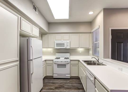 a kitchen with white cabinets and stainless steel appliances and a sink and refrigerator at Riverton of the High Desert Apartments, California