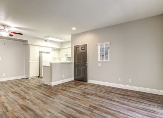 an empty living room with a kitchen and a ceiling fan at Riverton of the High Desert Apartments, 92392