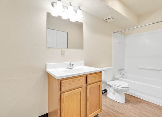A white sink with a wooden cabinet and a white toilet in a bathroom. at Winding Hills Apartments, Davenport , Iowa