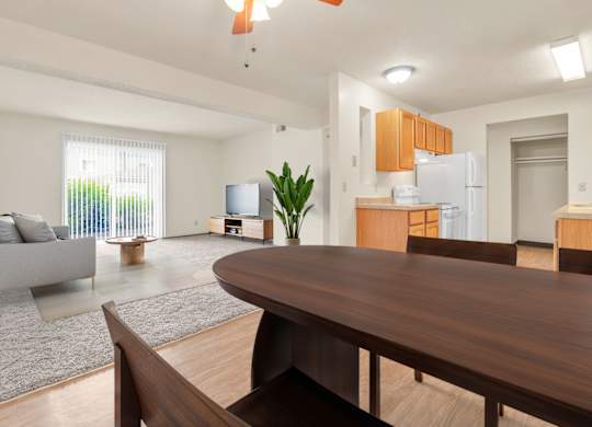 A modern living room with a grey couch, a wooden dining table, and a television. at Winding Hills Apartments, Davenport , IA
