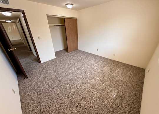 A carpeted room with a door and a mirror on the wall. at Winding Hills Apartments, Davenport , Iowa