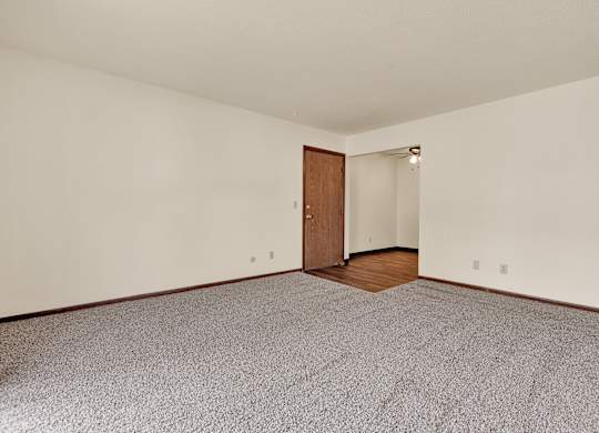 A room with a carpeted floor and a wooden door.at Windsor Crest Apartments, Davenport , Iowa