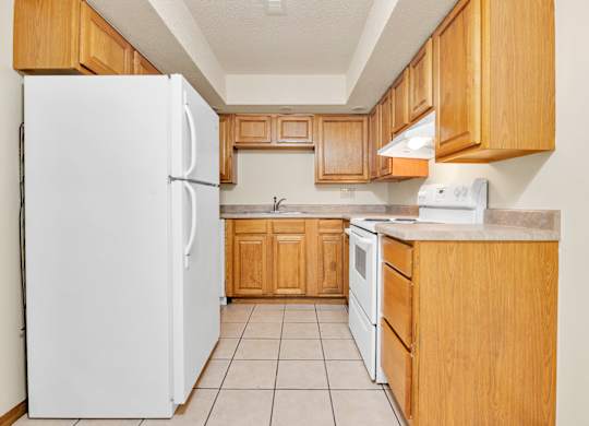 A white refrigerator stands in a kitchen with wooden cabinets and a white stove.at Windsor Crest Apartments, Davenport , Iowa