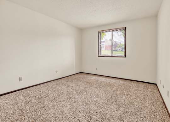 A room with a carpeted floor and a window. at Indian Ridge Apartments, Davenport, 52807