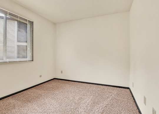 A room with a carpeted floor and a window with blinds. at Indian Ridge Apartments, Davenport