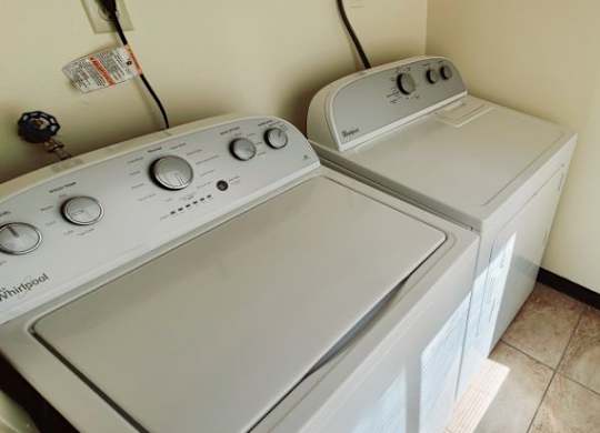 A white dryer and washer are stacked in a small laundry room. at Kimberly Club Apartments, Davenport