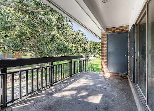 A balcony with a black railing and a view of trees and a brick building.