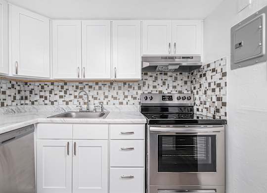 A kitchen with white cabinets and a black and white tiled backsplash.